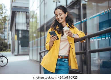 Shot of a fashionable young woman using her cellphone while walking through the city. Beautiful mid adult woman walking and texting message on mobile phone outside business center. - Powered by Shutterstock