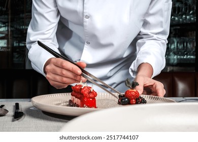 Shot of the female chef hold the kitchen tweezers and prepares dessert with red fruits for serving. Female chef.  - Powered by Shutterstock