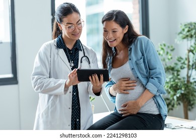 Shot of female gynecologist doctor showing to pregnant woman ultrasound scan baby with digital tablet in medical consultation.