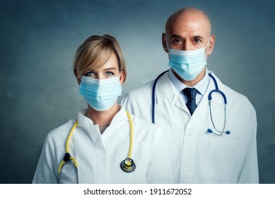 Shot of female and male doctors standing together at isolated background. Medical team. Doctors wearing face masks for prevention.
