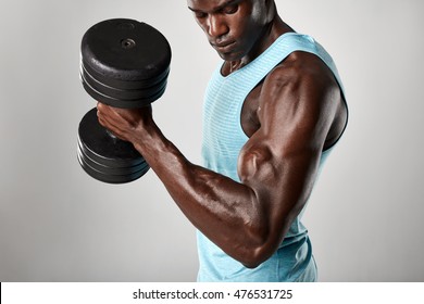 Shot of fit young man doing biceps curl with dumbbell against grey background. African fitness model exercising with heavy dumbbells. - Powered by Shutterstock