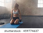 Shot of fitness woman sitting on exercise mat and looking at her triceps. Muscular woman working out at the fitness club.