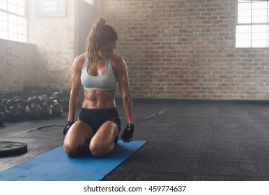 Shot of fitness woman sitting on exercise mat and looking at her triceps. Muscular woman working out at the fitness club.