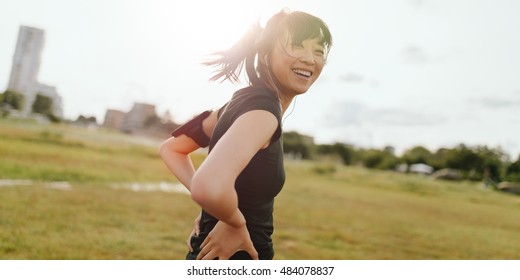 Shot of fitness young woman standing outdoors looking at camera and laughing. Female runner on field in morning.