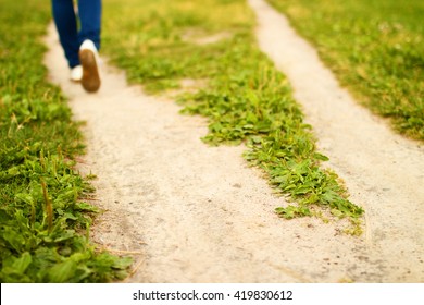 Shot of forked footpath among green grass and feet of person going away to the left, at sunny summer day. Divergence of paths on meadow. Concept of choosing of correct way and direction