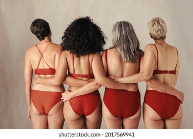 Shot Of Four Anonymous Women Of All Ages Embracing Their Natural And Aging Bodies. Group Of Women Embracing Each Other While Wearing Red Underwear And Standing Together In A Studio.