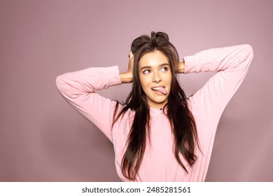 Shot of funny young long haired brunette woman showing tongue to camera, over pink background