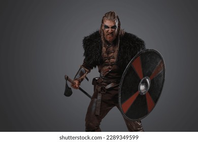 Shot of furious nordic warrior dressed in leather armor and fur against gray background. - Shutterstock ID 2289349599