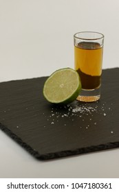 Shot glass with liquor, lime and salt served on blackboard plate white background.