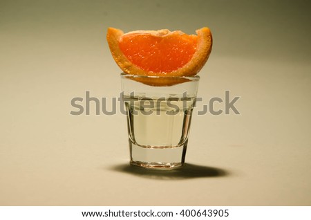 Shot glass with vodka or gin on the rocks served with a slice of fresh orange