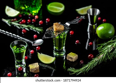 shot glasses with absinthe. Strong alcohol. Absinthe with brown sugar, cranberries, ice cubes and lime slices om dark background.