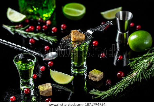 shot glasses with absinthe. Strong alcohol.\
Absinthe with brown sugar, cranberries, ice cubes and lime slices\
om dark background.