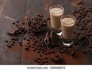 Shot Glasses Of Irish Cream Baileys Liqueur With Coffee Beans And Powder With Dark Chocolate On Dark Wood Background. Macro