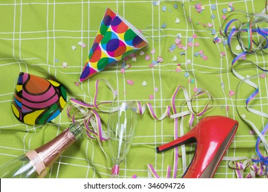 Shot Of A Green Tablecloth After A Party Celebration With Confetti, Empty Bottle And Glass Of Champagne, Party Popper And Red Court Shoe.