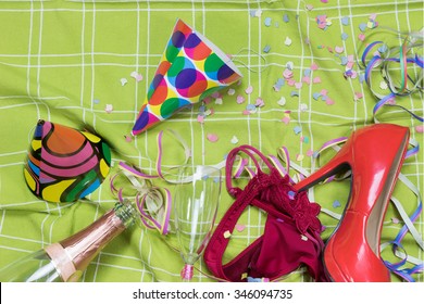 Shot Of A Green Tablecloth After A Party Celebration With Confetti, Empty Bottle, Glass Of Champagne With Lipstick Imprint, Party Popper, Red Court Shoe And Rd Panties.