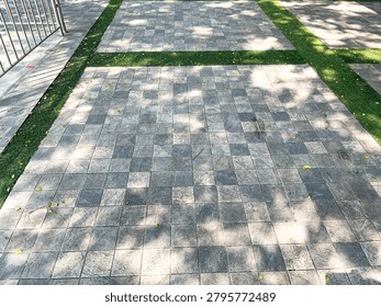 Shot of a ground level of a pathway, constructed with grey square paving stones that are arranged in a checkered tiles pattern. With some grass borders are also seen. In the distance, there's a partially shown entry line silver bar gates. Sunlight ray fliters also shone overhead the greens evoking a beautiful fresh scene of a summertime.