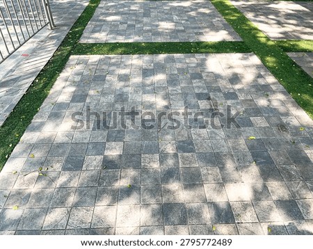 Shot of a ground level of a pathway, constructed with grey square paving stones that are arranged in a checkered tiles pattern. With some grass borders are also seen. In the distance, there's a partially shown entry line silver bar gates. Sunlight ray fliters also shone overhead the greens evoking a beautiful fresh scene of a summertime.