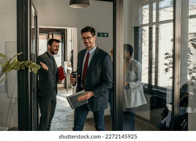 Shot of a group of a businessman holding the door while his coworkers enter the office. Confident young business people working together in the office. - Powered by Shutterstock