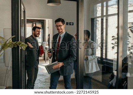 Shot of a group of a businessman holding the door while his coworkers enter the office. Confident young business people working together in the office.
