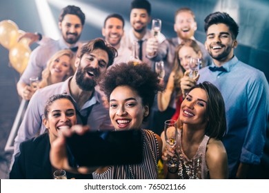 Shot of a group of friends taking selfies on a mobile phone at a party - Shutterstock ID 765021166