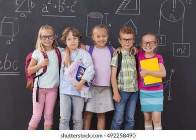 Shot Of A Group Of Primary School Students Standing Against A Blackboard Wall In A Classroom