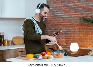 Shot Of Handsome Mature Man Cooking While Using Mobile Phone In The Kitchen At Home.