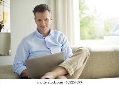 Erschossen Sie einen gut aussehenden Mann mit seinem Laptop und entspannen Sie sich auf dem Sofa zu Hause. 