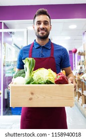 Shot Of Handsome Sellman Holding A Box With Fruits And Vegetables In Health Grocery Shop