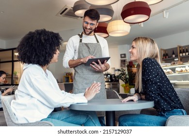 Shot of handsome smiling waitress using application on digital tablet computer to order what the two girls want for breakfast in a pastry shop.