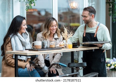 Shot of handsome waiter serving toast for brunch to two modern girls sitting on the terrace on the healthy coffee shop terrace. - Powered by Shutterstock