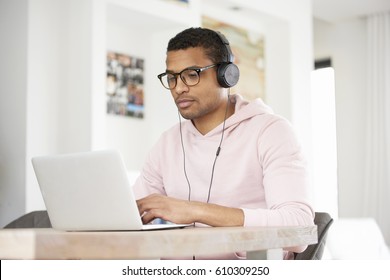 Shot of a handsome young Afro American man using his laptop while listening music and relaxing at home. - Shutterstock ID 610309250