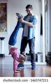 Shot Of Handsome Young Father Helping To Pretty Daughter To Doing Cartwheel At Home.