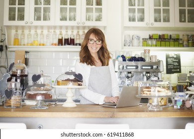 Shot Of A Happy Coffee Shop Owner Using A Laptop Behind The Counter In A Bistro. Small Business. 