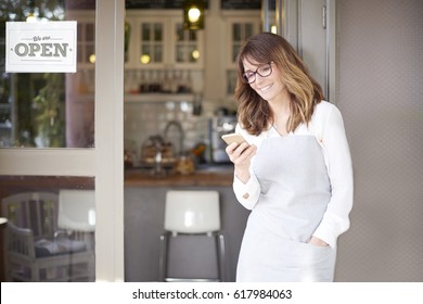 Shot of a happy confident cafe owner standing at doorway and text messaging. Small business.