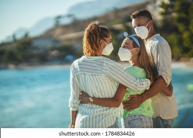 Shot of a happy embraced family with protective N95 mask spending time on the seaside at corona pandemic. They are having self-isolation in nature. - Powered by Shutterstock