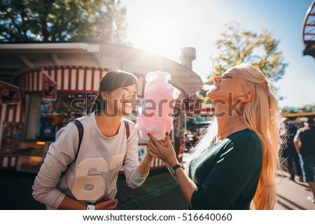 Shot of happy female friends in amusement park eating cotton candy. Two young women enjoying a day at amusement park.