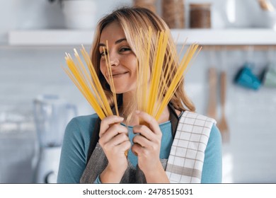 Shot of happy funny young woman showing raw spaghetti to the camera in the kitchen at home - Powered by Shutterstock