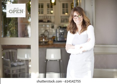 Shot of a happy mature coffee shop owner standing with arms crossed at doorway while looking at camera and smiling. Small business.