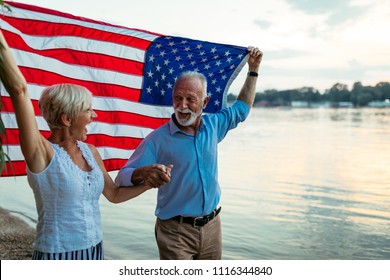 Shot of a happy senior couple walking by the river with an American flag. - Powered by Shutterstock