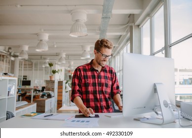 Shot of happy young man working on desktop computer in modern workplace. Young entrepreneur working at start up.
