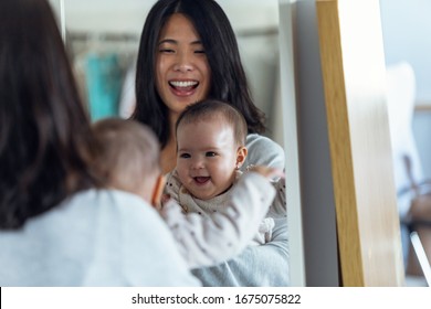 Shot of happy young mother with her little girl looking in the mirror while smiling at home. - Powered by Shutterstock