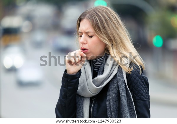 Shot of\
illness young woman coughing in the\
street.