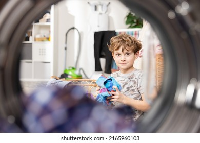 Shot from inside washing machine view of bathroom, laundry room. Little boy sits focused and throws towel towards drum, fooling around, playing basketball while cleaning house. - Powered by Shutterstock