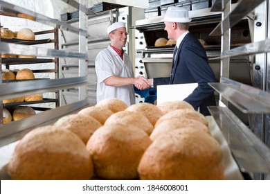 A shot of an inspector shaking hands with bakery owner in a bakery with loaves of bread in the foreground. - Powered by Shutterstock