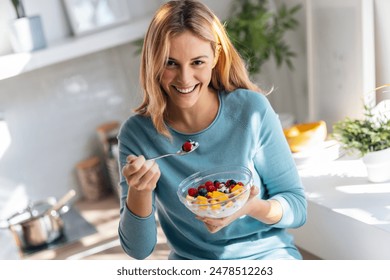 Shot of kind beautiful woman eating a healthy fruit bowl while sitting on the table in the kitchen at home - Powered by Shutterstock