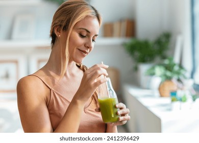 Shot of kind woman drinking a healthy green smoothie standing in the living room at home. - Powered by Shutterstock