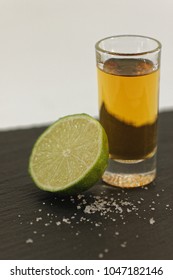 Shot of liquor with lime slice and a pinch of salt served on blackboard plate.