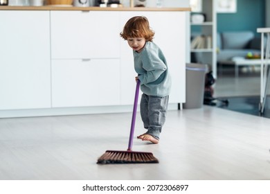 Shot of little cute boy sweeping and cleaning the floor of the kitchen at home.