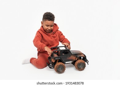 Shot of little dark skinned African boy wearing orange tracksuit playing toy car against white background in studio