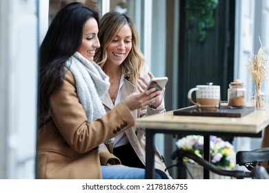 Shot of lovely girls couple sharing a brunch together while talking and looking the smartphone on the healthy coffee shop terrace. - Powered by Shutterstock